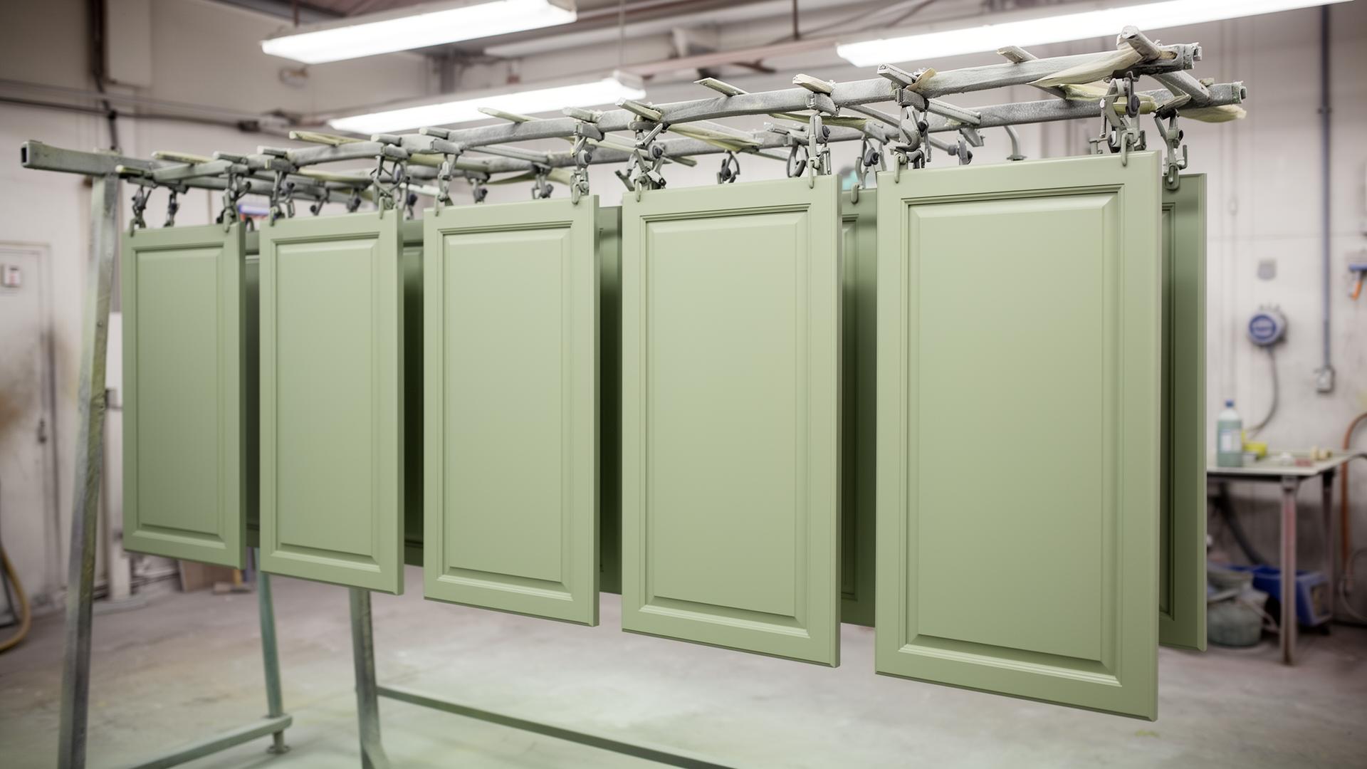 Sage-green cabinet doors hanging on a spray rack drying in our DFW paint shop