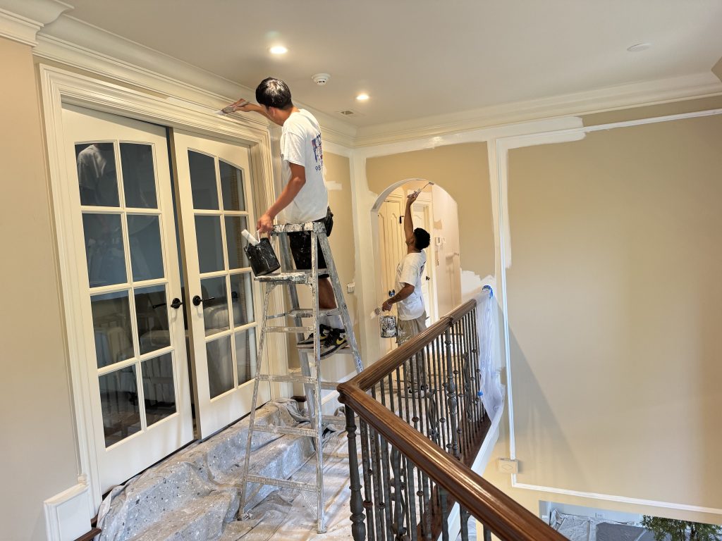 Crew patching drywall and rolling paint on the same wall